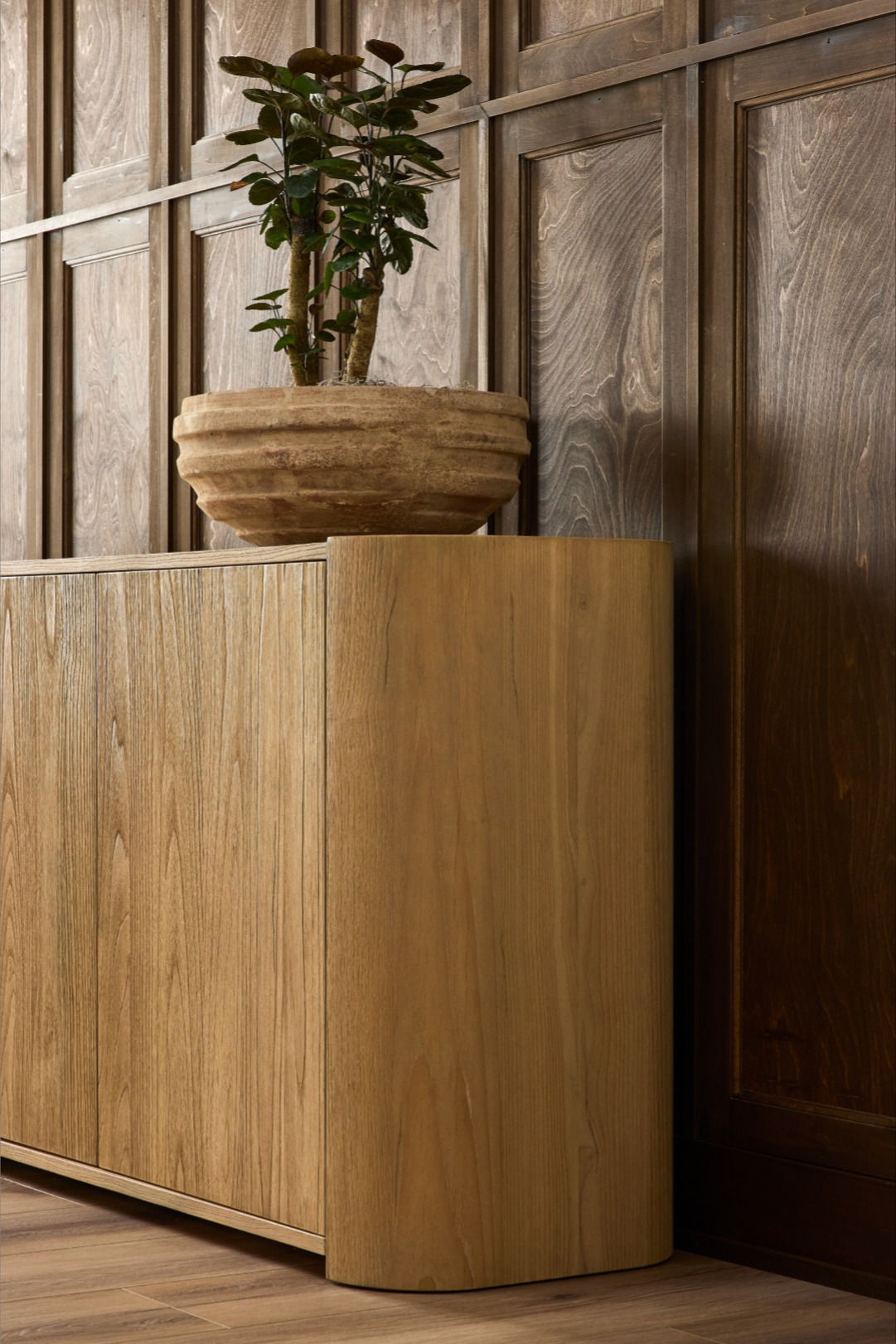 Light brown sungkai wood sideboard with rounded corners and four push-latch doors, topped with a plant.