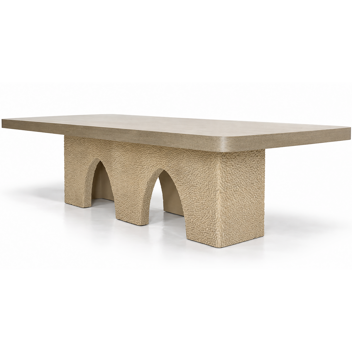 A modern rectangular table with a smooth, matte beige top and a textured, blocky base featuring three arch-like supports, shown on a clean white background.