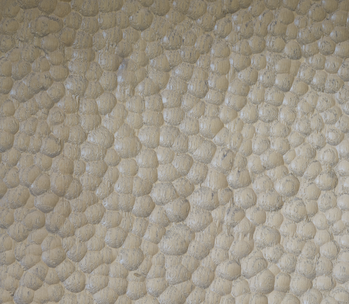 A close-up of a textured surface featuring a repeating pattern of small, raised beige and cream circular bumps, resembling a pebbled or bubbled material.