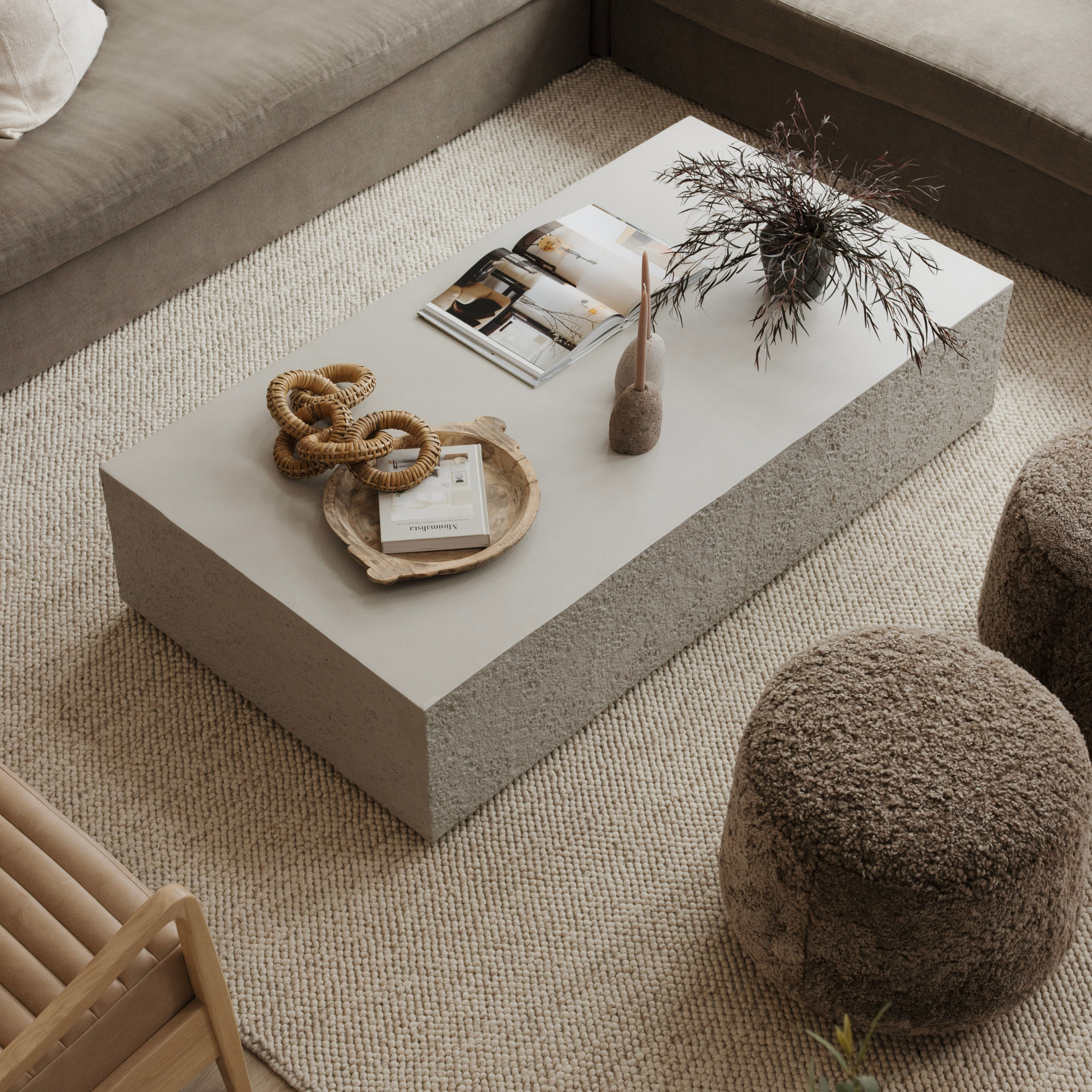 Lena Ottoman: Round, textured brown poly/wool ottoman with oak bun feet, next to a coffee table.