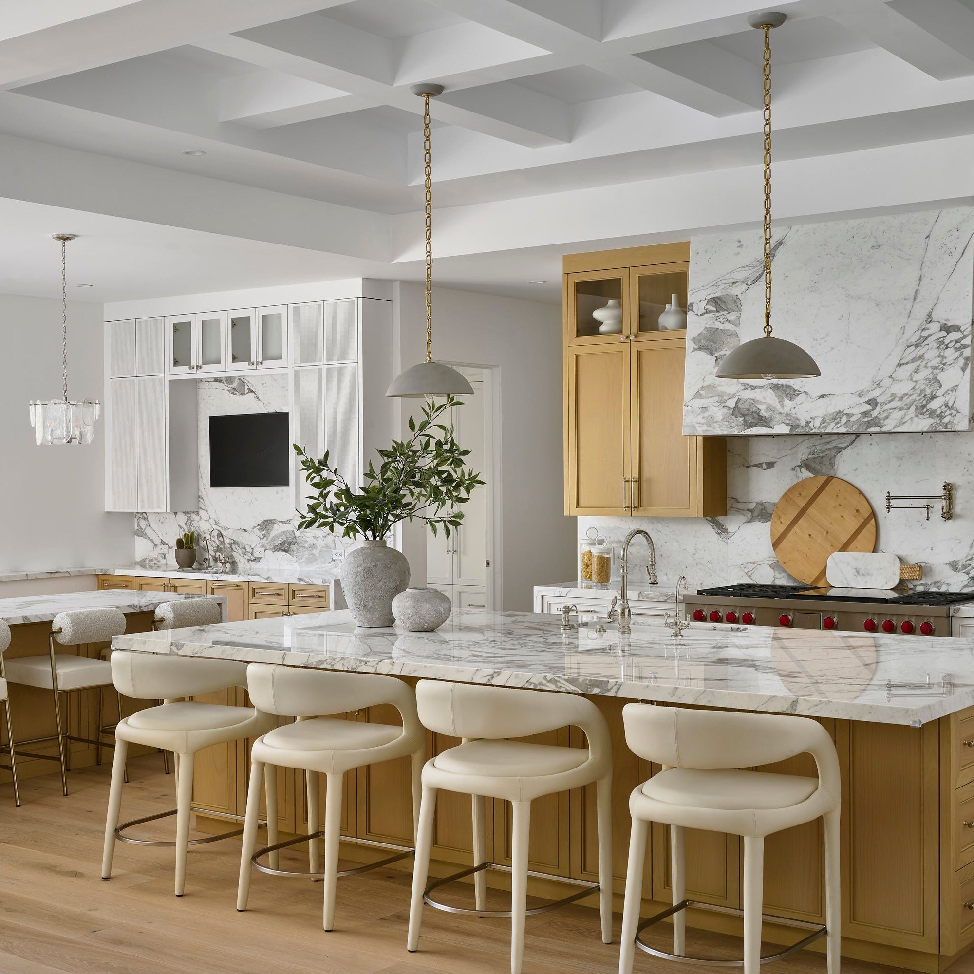 A modern kitchen island with a white marble countertop and backsplash, surrounded by cream bar stools, set in a bright kitchen with light wood cabinets and white walls.
