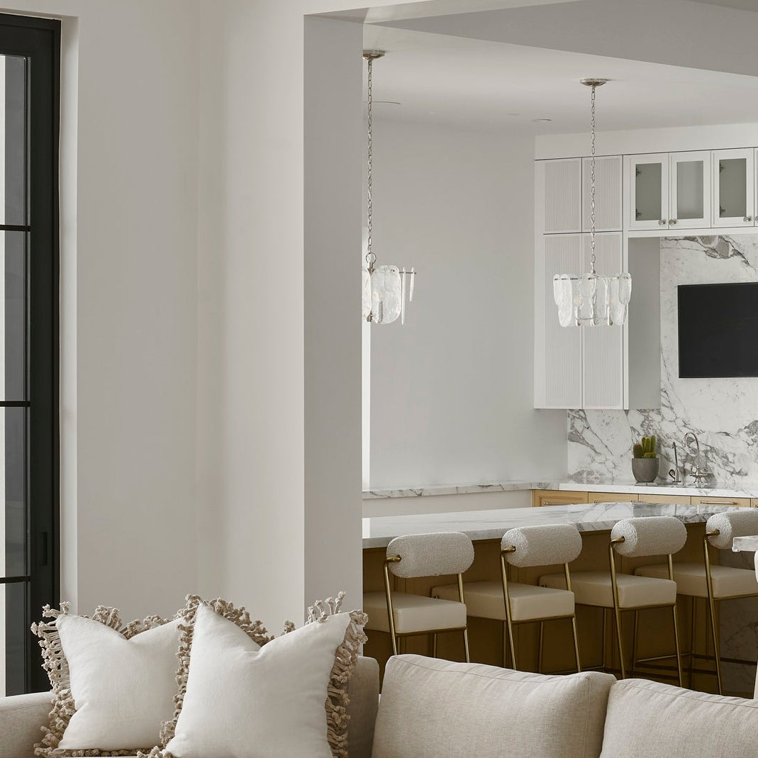 A large beige sectional sofa in a bright, modern open-concept living room with light wood floors, a kitchen island, and bar stools in the background.
