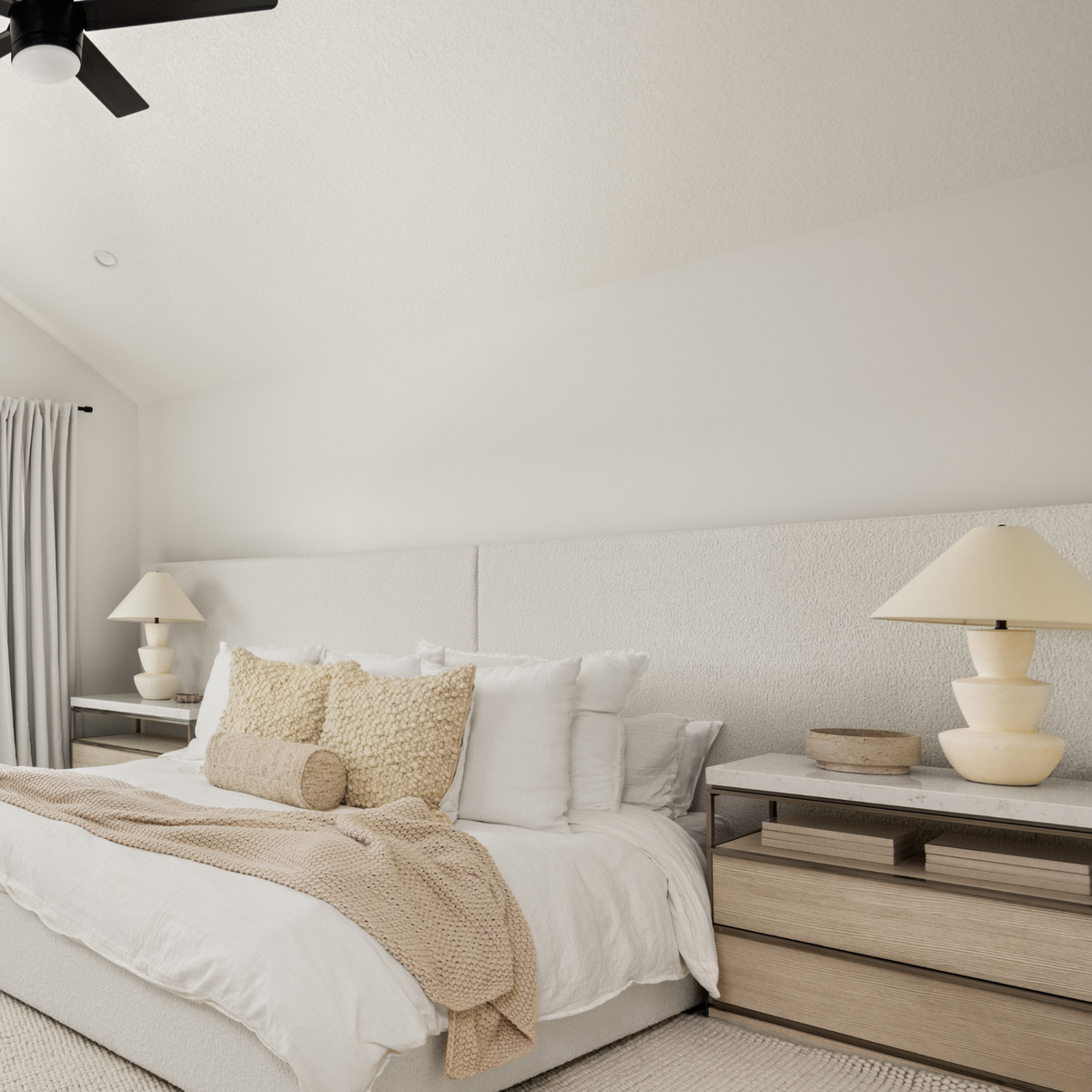 A modern bedroom featuring a bed dressed in white linens with textured beige pillows and a beige knit throw blanket, flanked by matching light wood nightstands with a marble top.