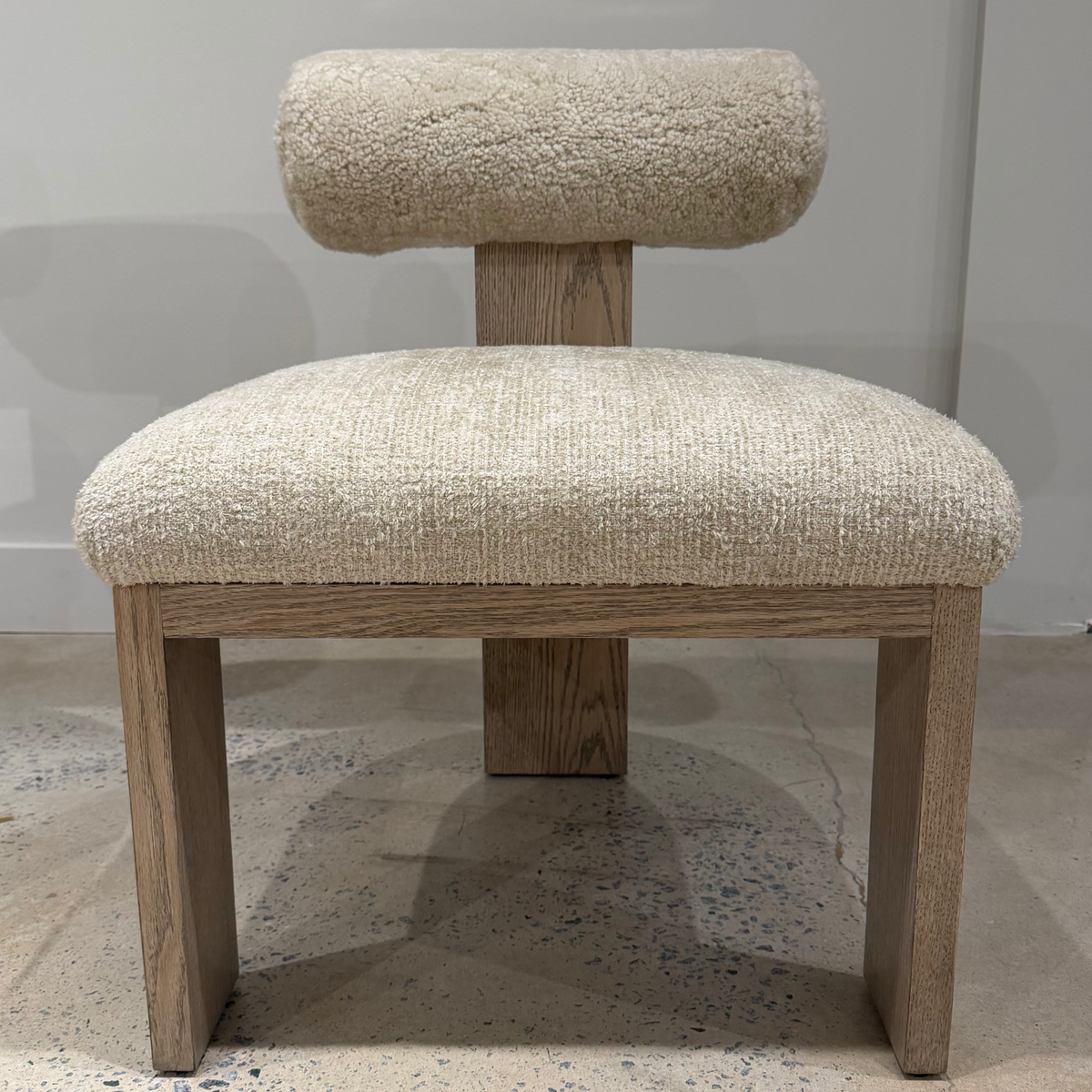 Front view of the Yucca Dining Chair with a wide cream upholstered seat, textured curved backrest, and wood legs.