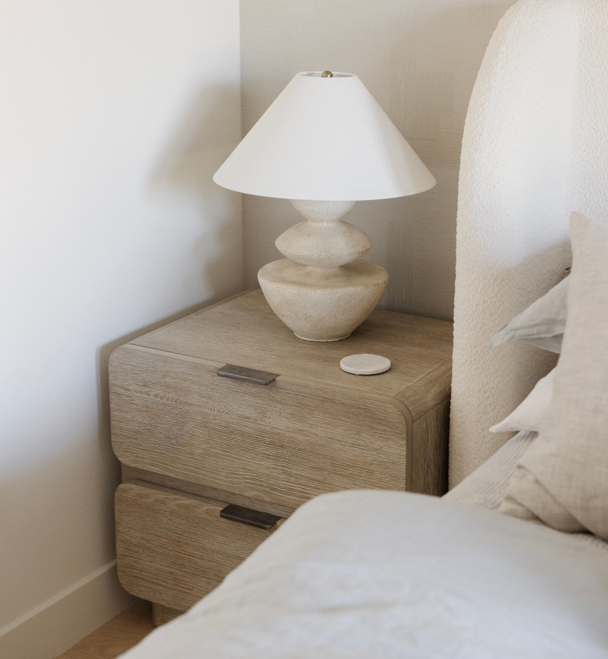 Wooden nightstand with a lamp next to a bed in a bedroom setting