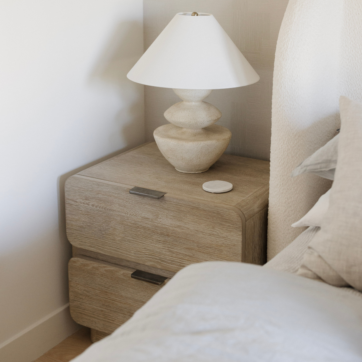 Wooden nightstand with a lamp next to a bed in a bedroom setting