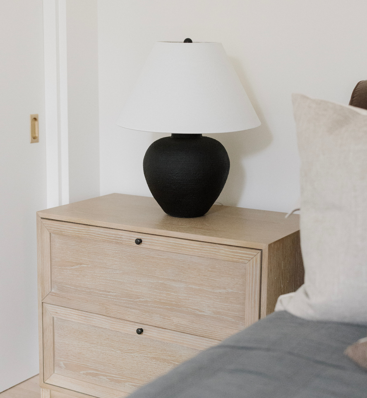 Black lamp on a wooden nightstand next to a bed with pillows