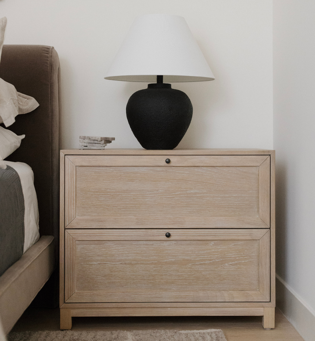Wooden nightstand with a black lamp next to a bed in a bedroom setting.