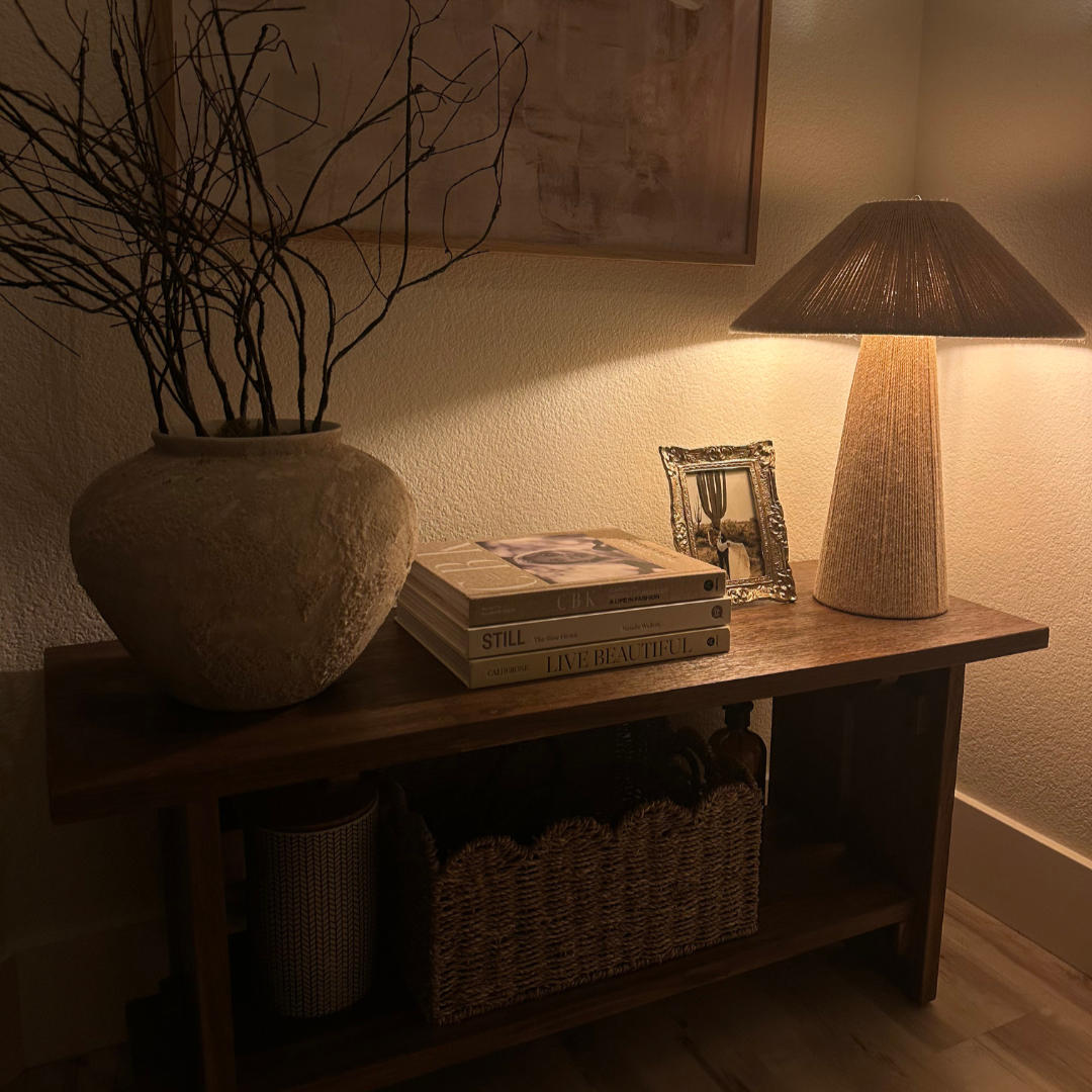 Nestled corner with a lamp, vase with branches, books, and a basket on a wooden shelf.