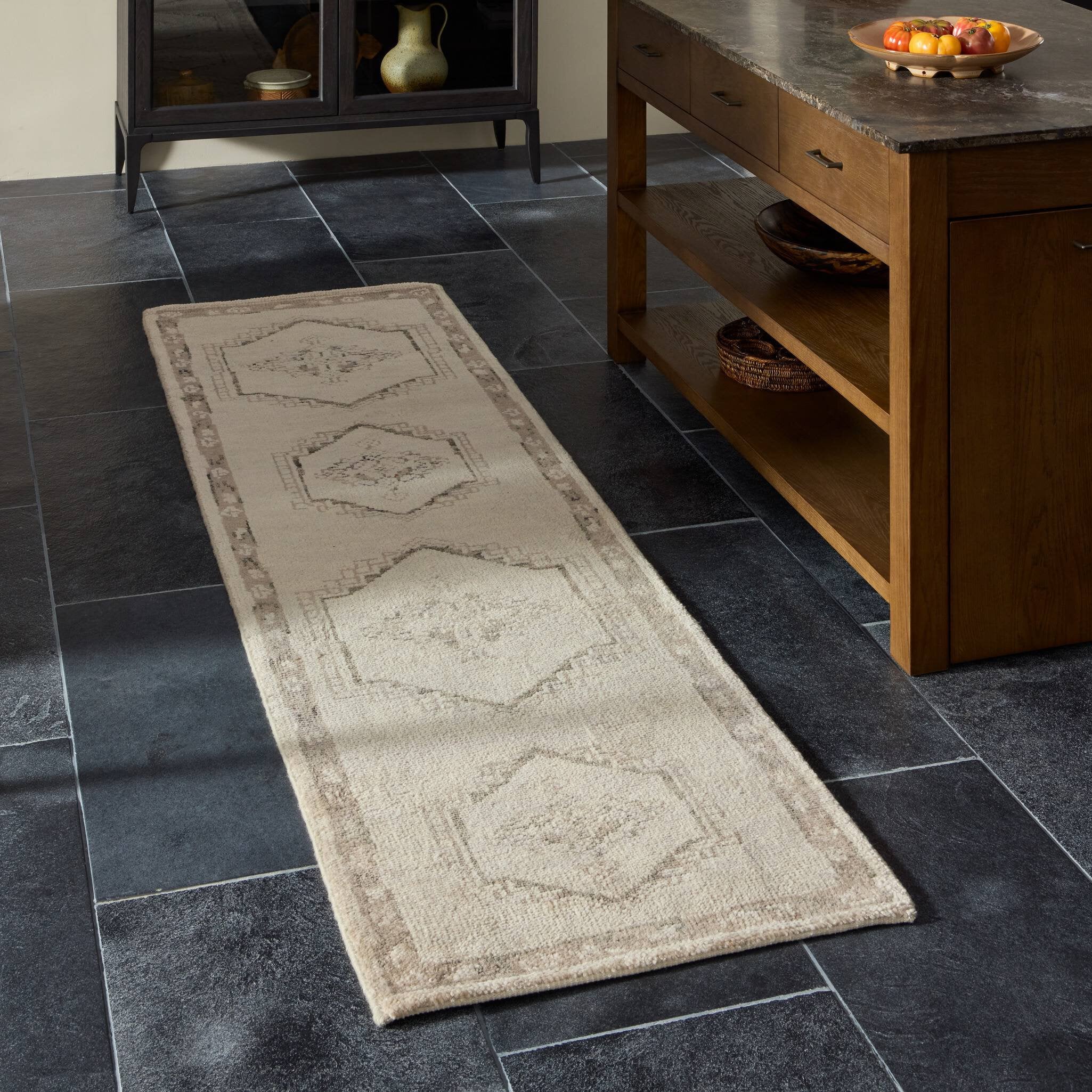 Long rectangular beige rug on a dark tiled floor with a wooden cabinet in the background.