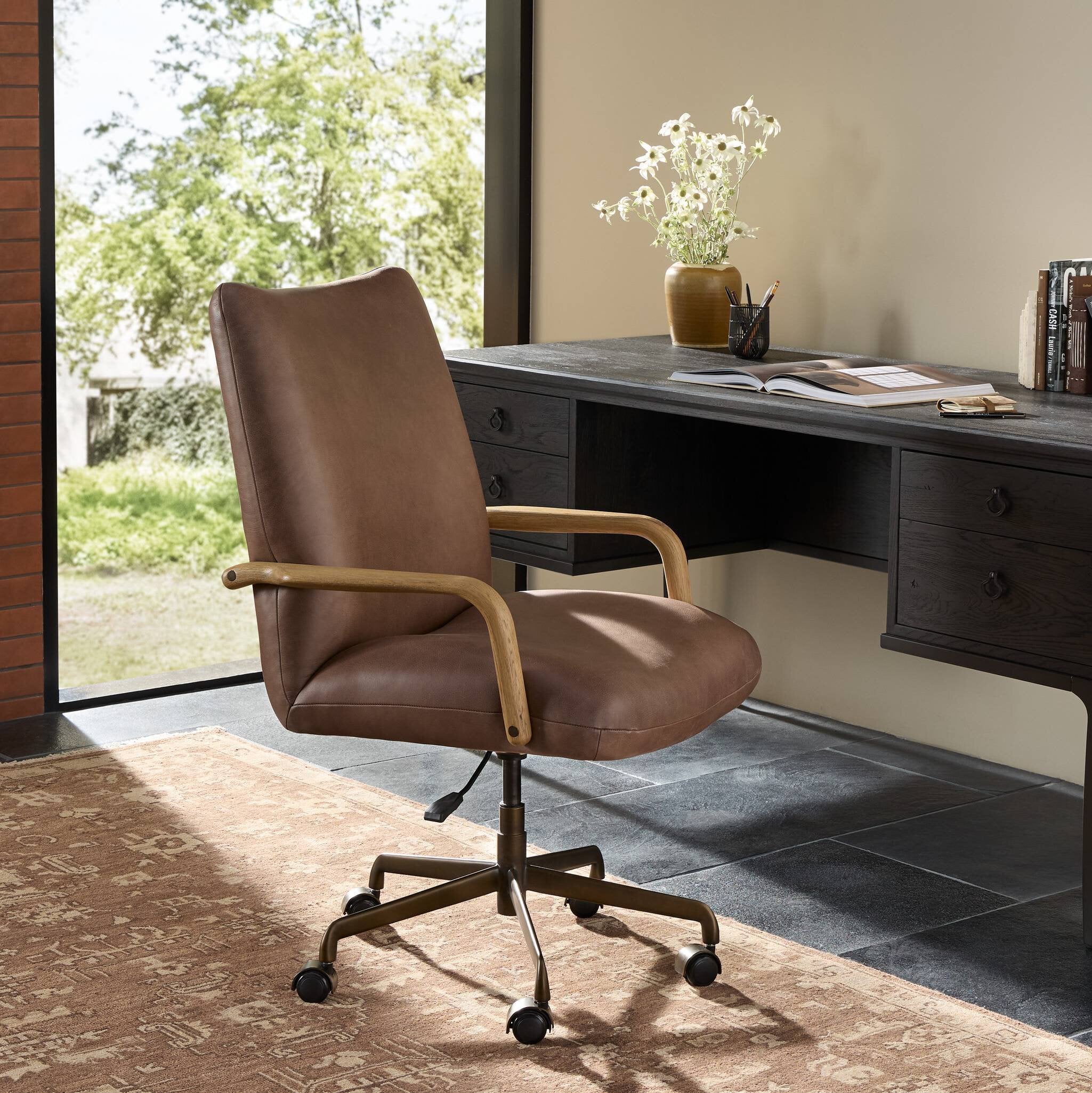 Sammy Desk Chair in brown leather with wooden paddle arms and brass base at a dark desk.