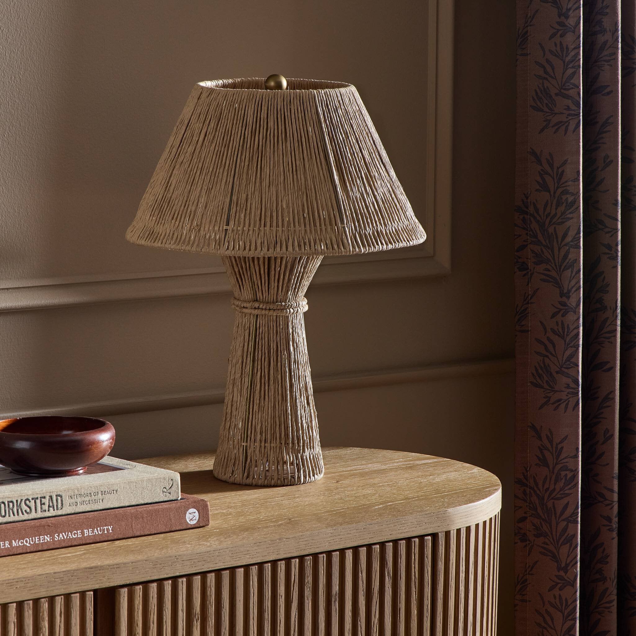 Textured table lamp on a wooden side table with books and a decorative bowl.