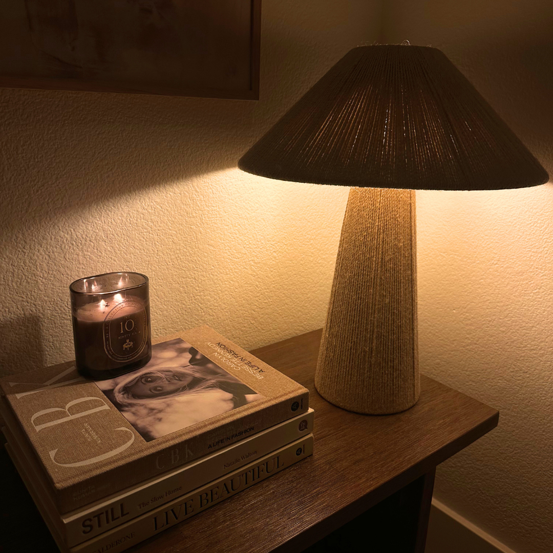 Lamp casting a warm glow on a stack of books with a candle on a wooden surface.