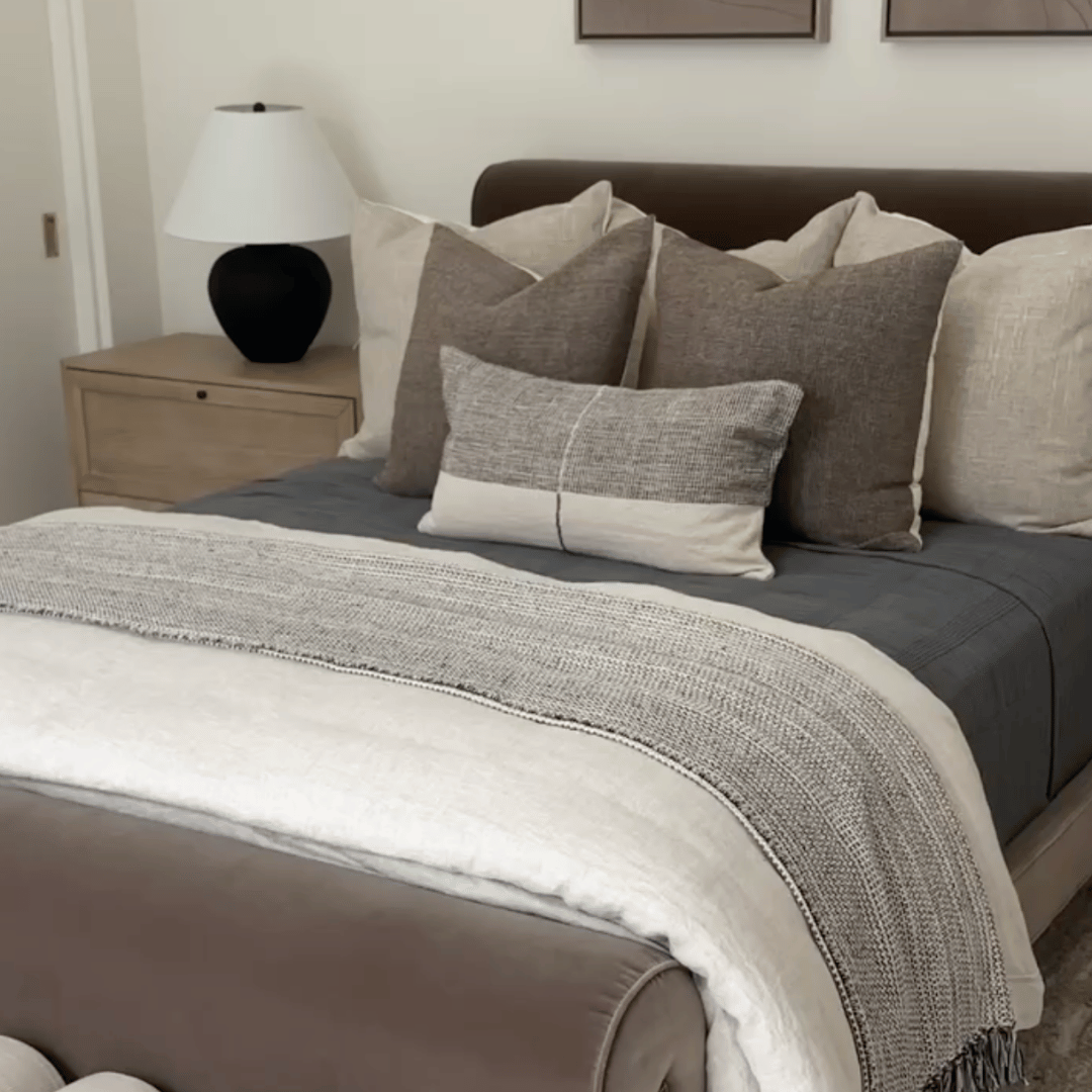 Neatly made velvet bed with gray and brown pillows and a blanket in a bedroom setting.