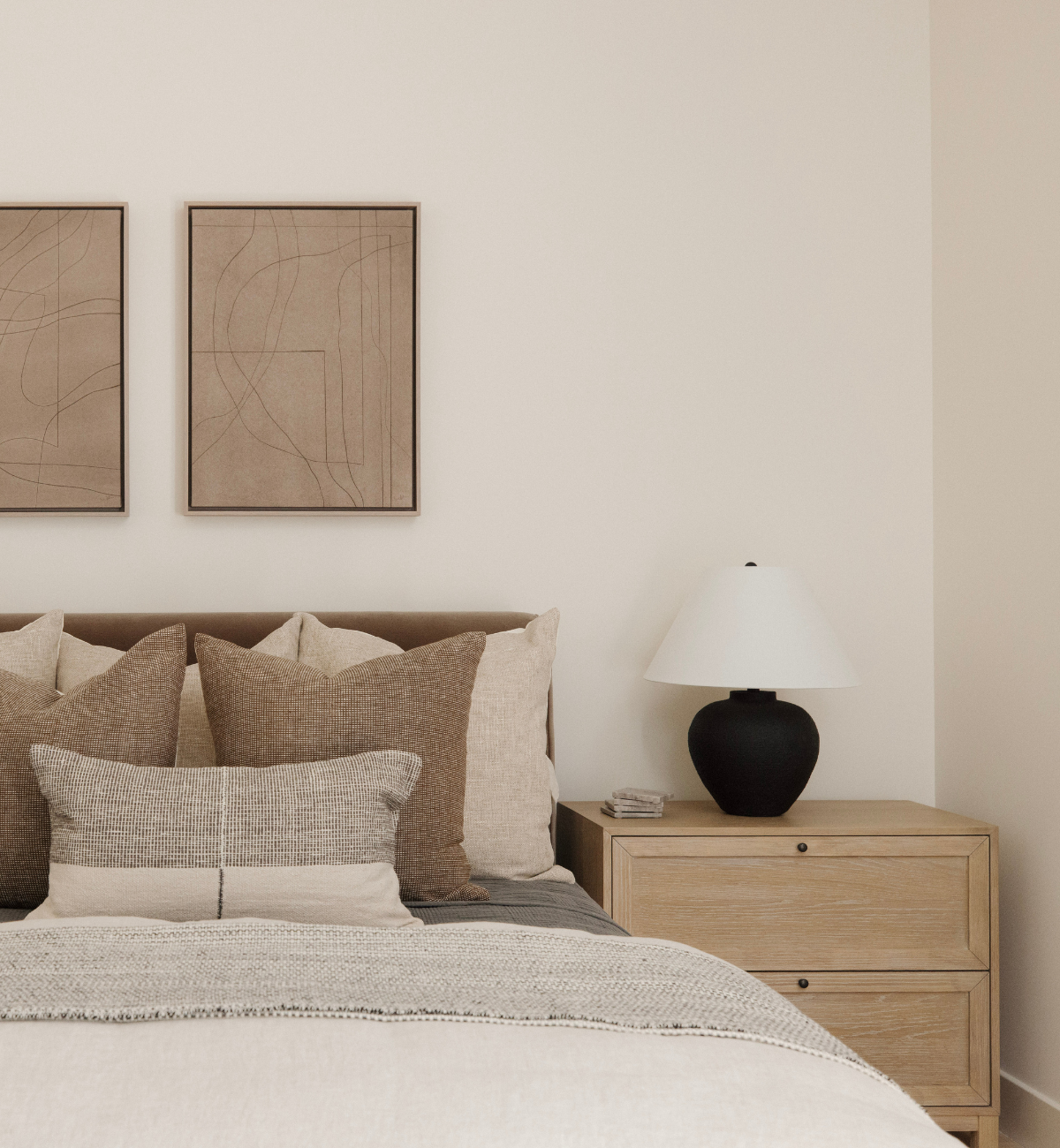 Neatly made bed with pillows and a lamp on a nightstand in a bedroom setting.