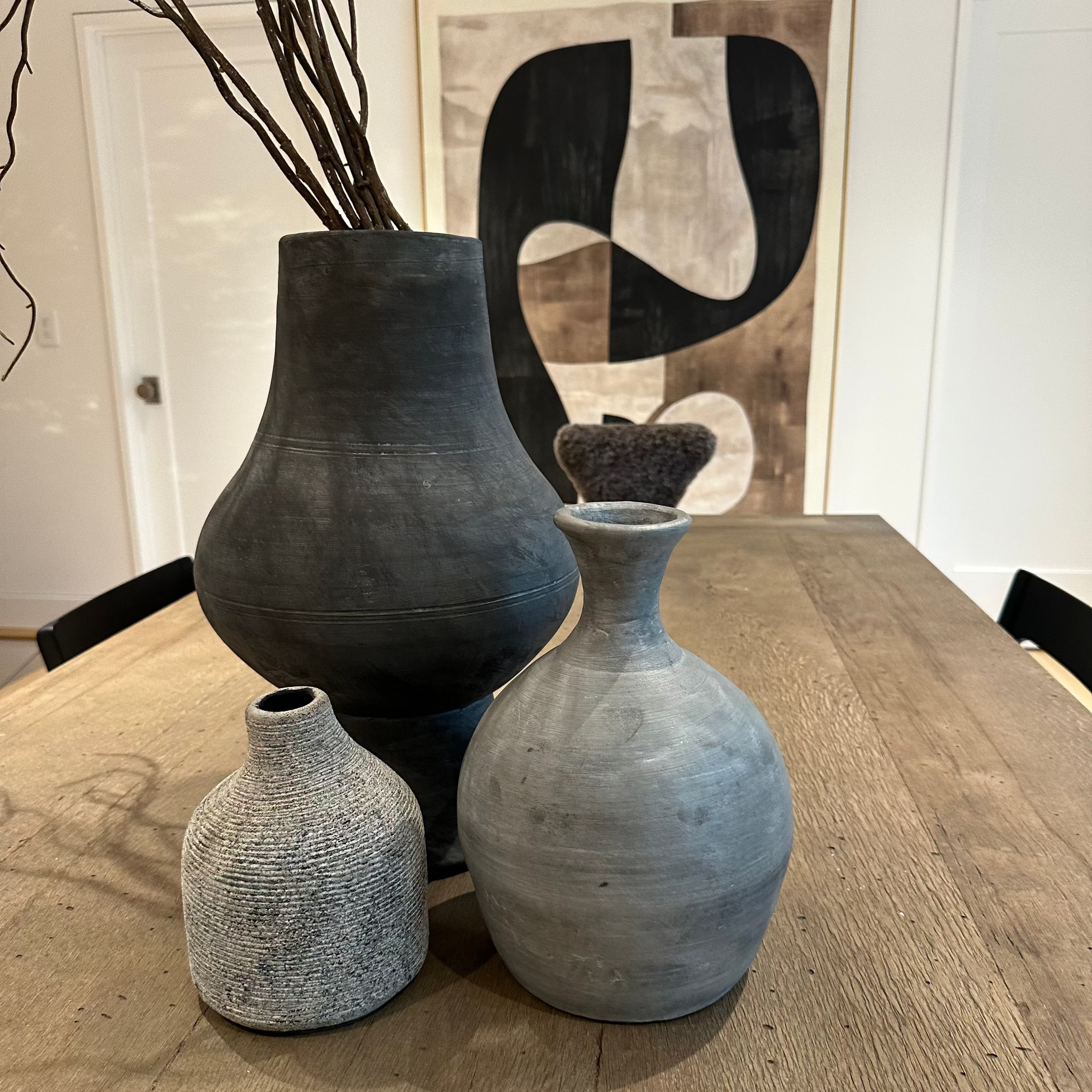 Three ceramic vases on a wooden table with abstract art in the background