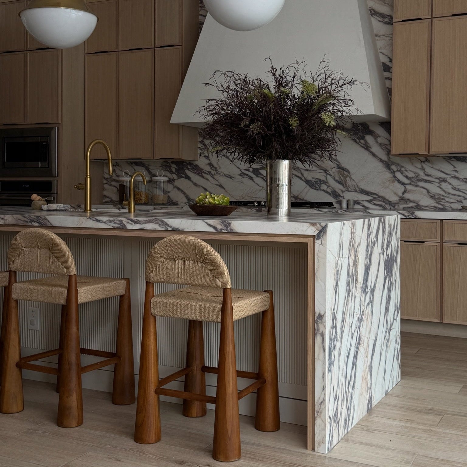 Modern kitchen with marble island, wooden stools, and gold pendant lights.
