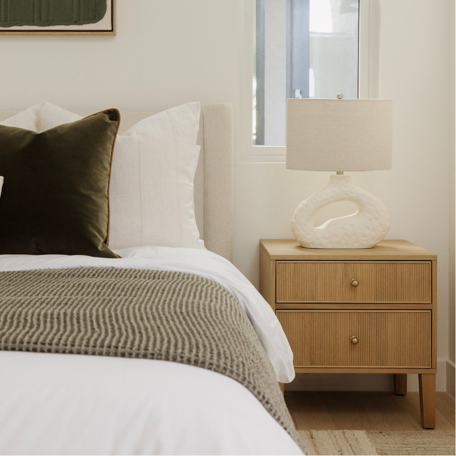Bedroom with a bed featuring a brown pillow and beige blanket, next to a wooden nightstand with a lamp.