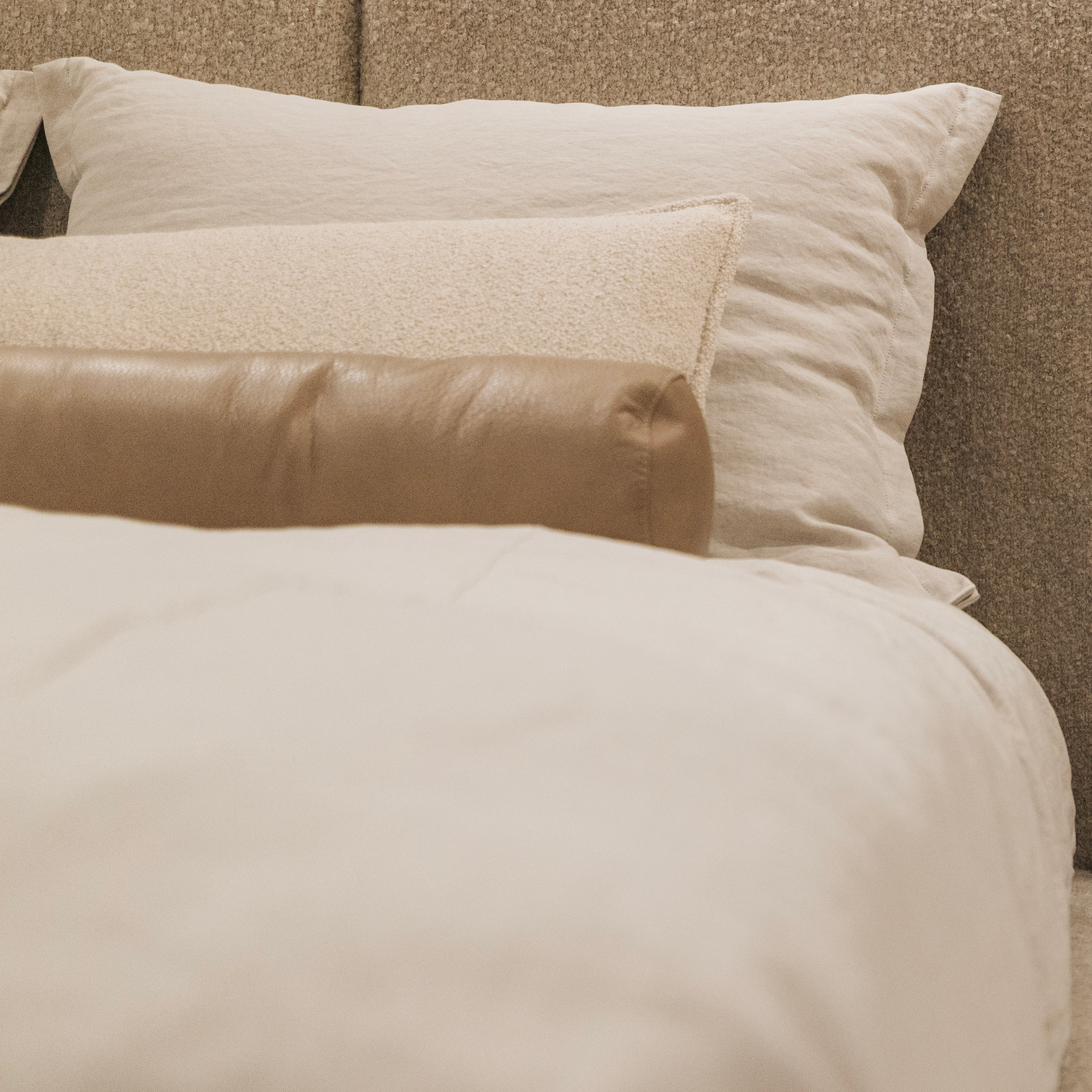Close-up of beige bedding with textured pillows on a bed.