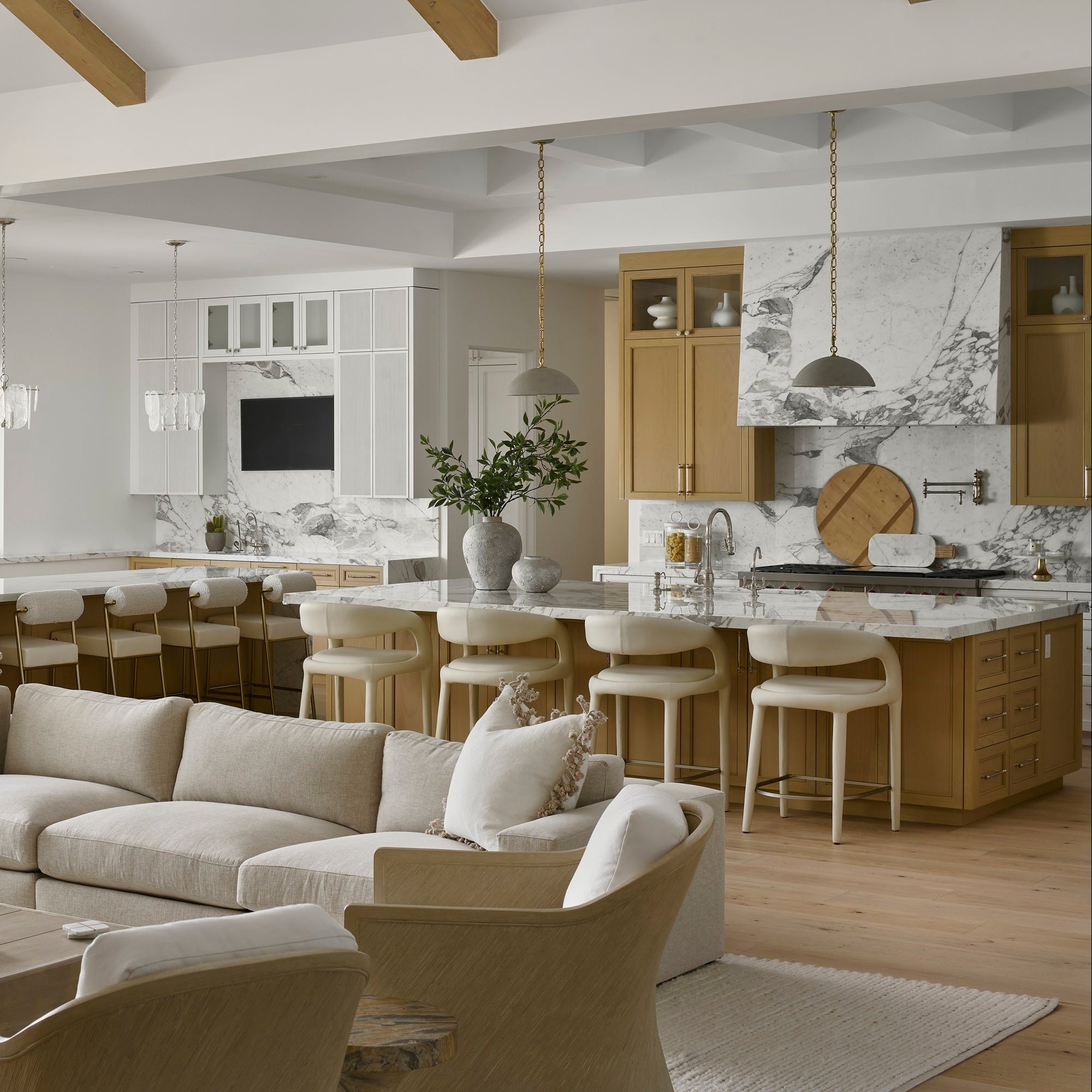 A large beige sectional sofa in a bright, modern open-concept living room with light wood floors, a kitchen island, and bar stools in the background.