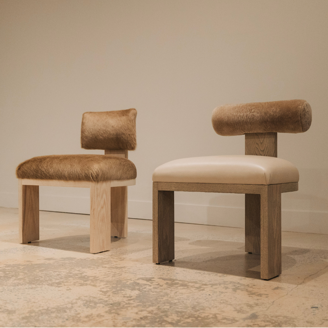 Two dining chairs with wooden frames, one upholstered in brown hair-on-hide and one with a cream leather seat and hide bolster back