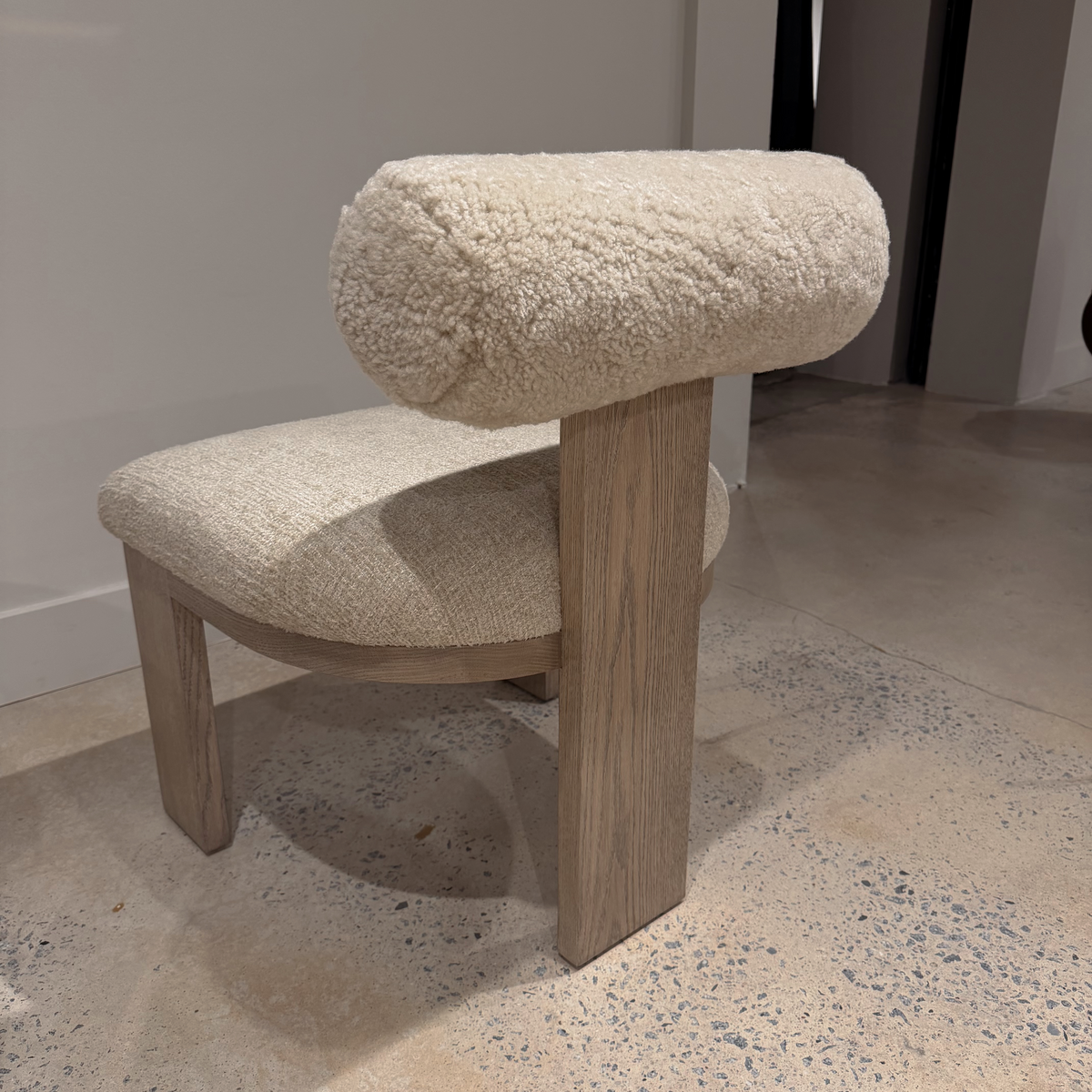 Rear left view of the Yucca Dining Chair with a textured cream backrest, upholstered seat, and broad wood back support.